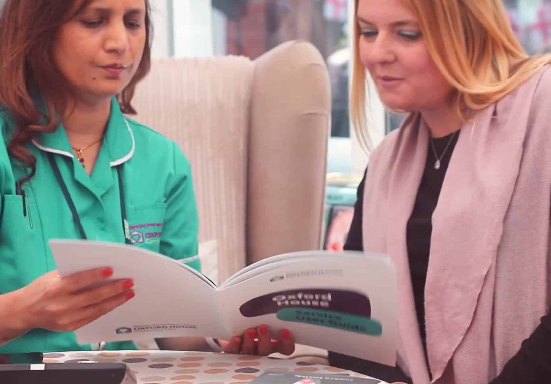 Two women engaged in conversation while looking through a booklet together.