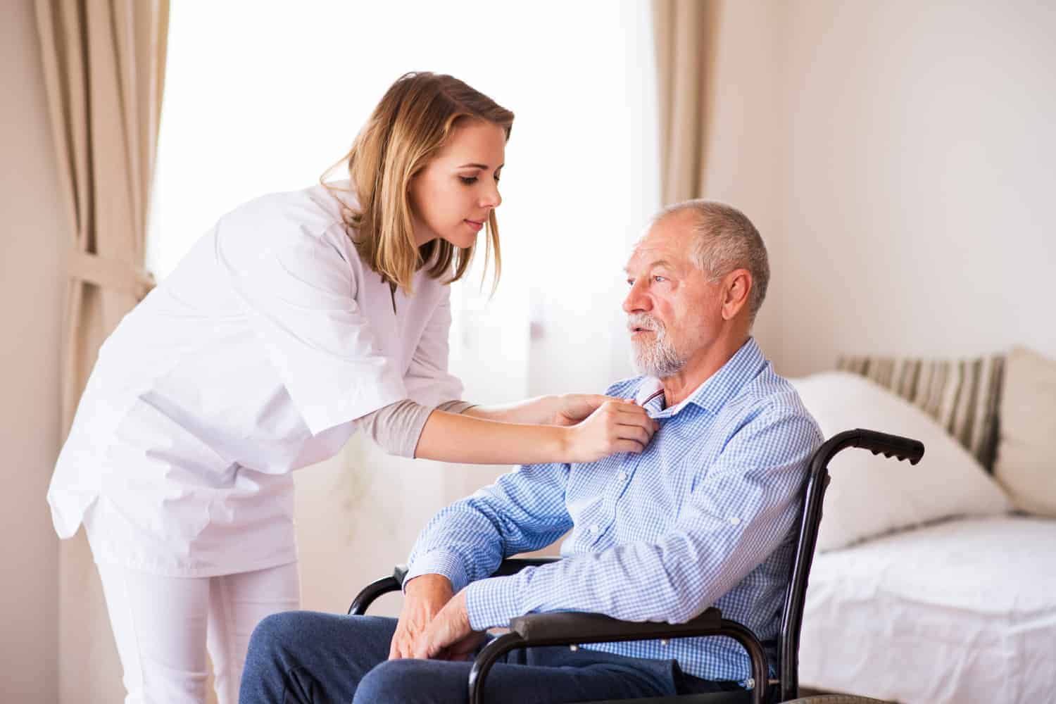 A Care Worker attentively attending to an elderly man in a wheelchair, helping to button up his shirt.